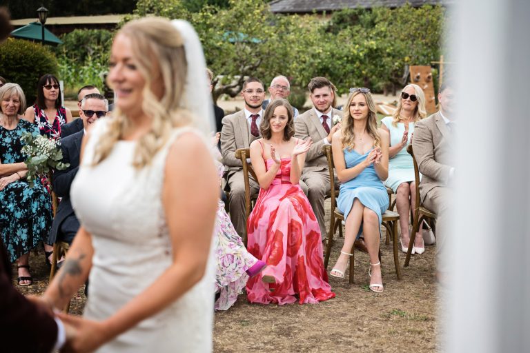 weddings guests clap in celebration of the bride (just out of focus) and groom getting married