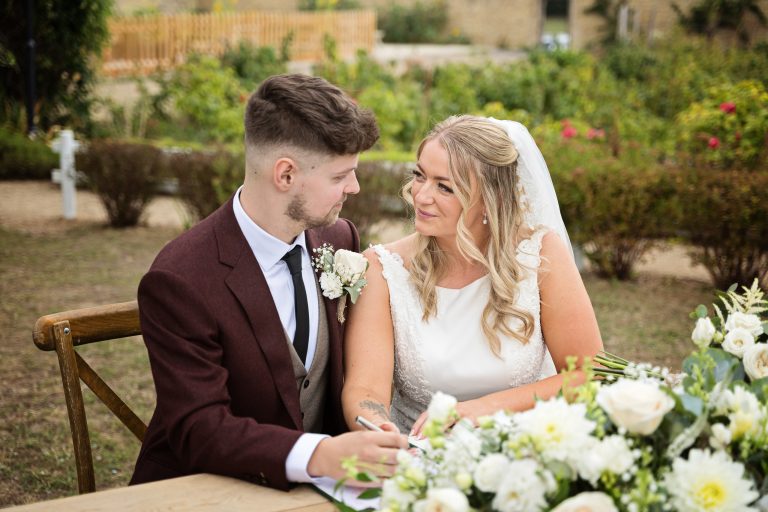 bride and groom look at each other as they sign the wedding register