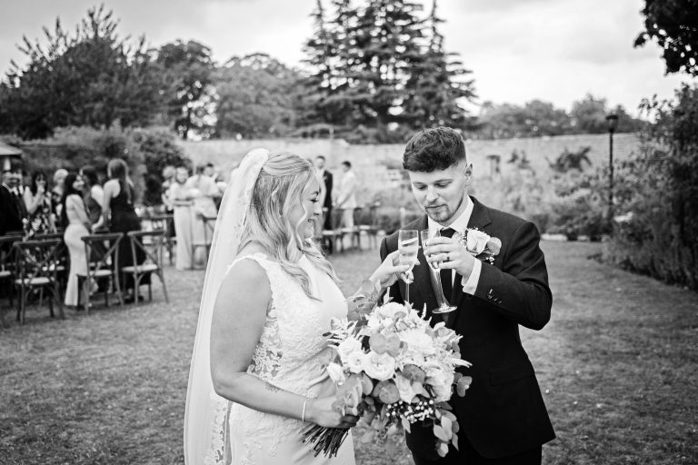 b&w image of a bride & groom celebrating after getting married by chingging two champagne glasses together