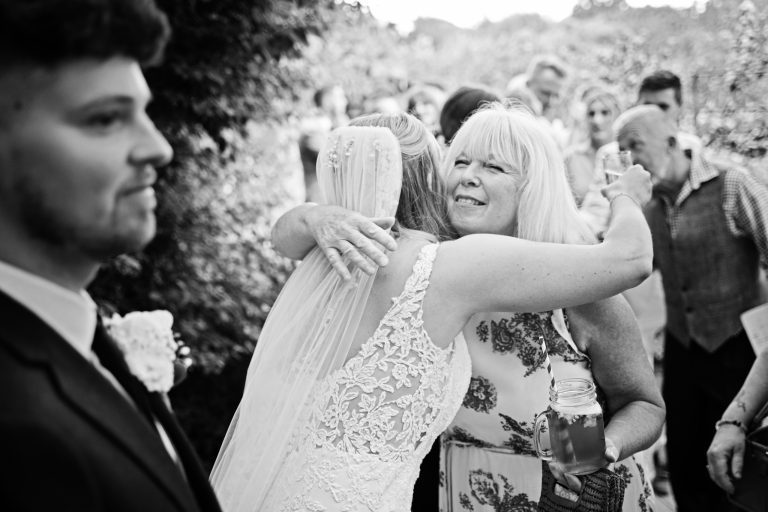 b&w image of a bride being hugged by a wedding guest