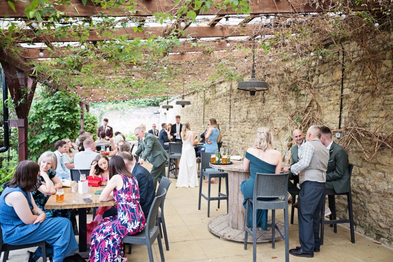 Wedding guests sit and chat around tables under a green canopy