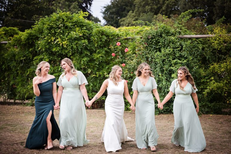 bridesmaids and bride holding hands, and smiling and laughing at each other