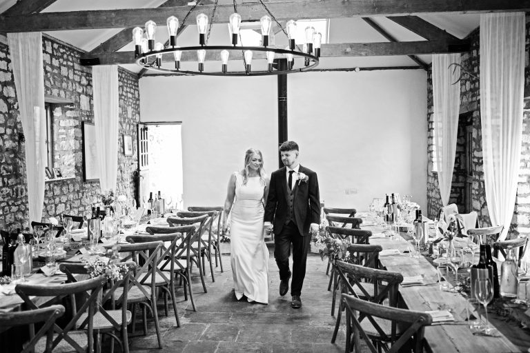 b&w image of bride and groom smiling at each other as they walk through their wedding breakfast