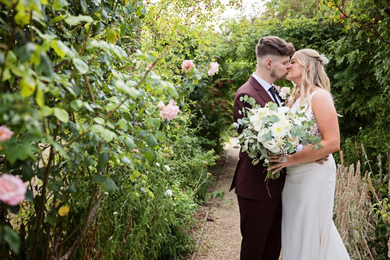 bride and groom kissing each other as they stand in a rose garden.