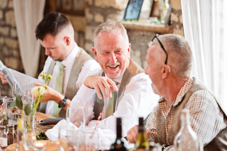 Candid photo of two older brothers laughing whilst sat at a wedding table