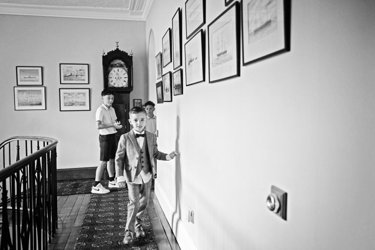 B &W image of boys dressed up for a wedding playing in a Georgian manor house - they look mischievous