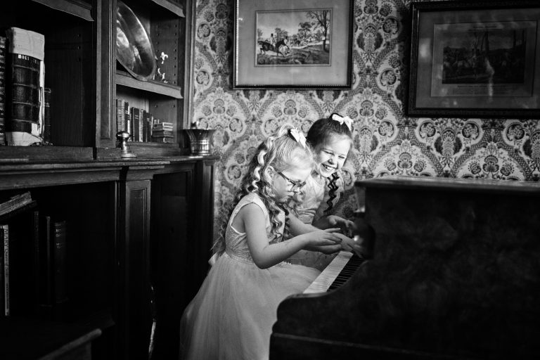 A b&W fun image of two flower girls -one laughing and the other one is playing the piano