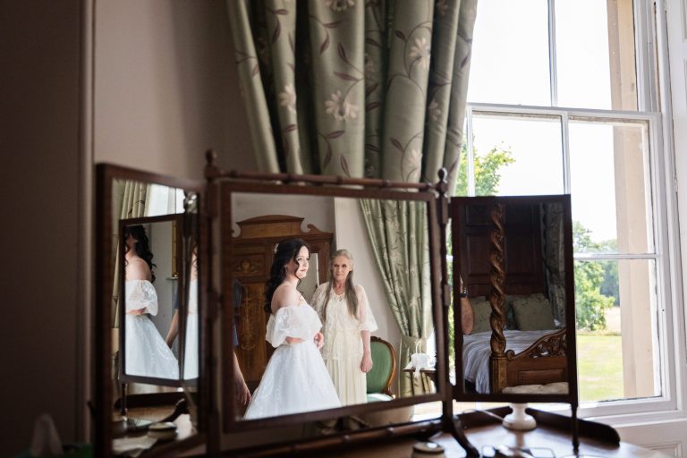 A reflection of a bride in her wedding dress and her mum watching.