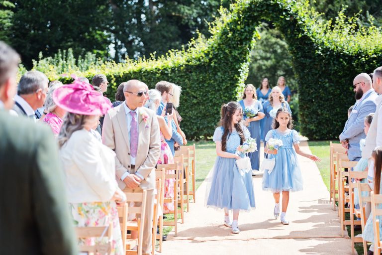 Flower girls walking down the wedding isle. Guests watching the outdoor ceremony