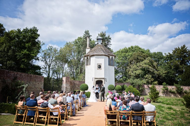 A bride and groom say their wedding vows next to a castle. Wedding guests are seated watching them