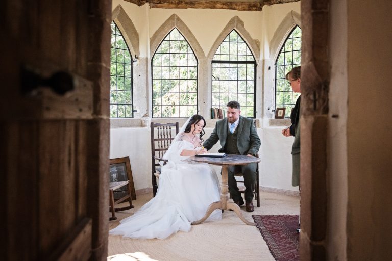 looking through a partially opened door in a castle a bride signs the wedding register
