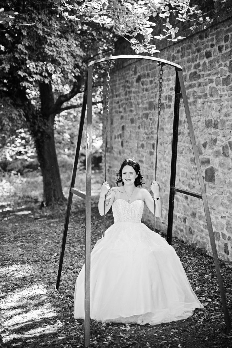 A b&w image of a bride smiling, sitting on a swing