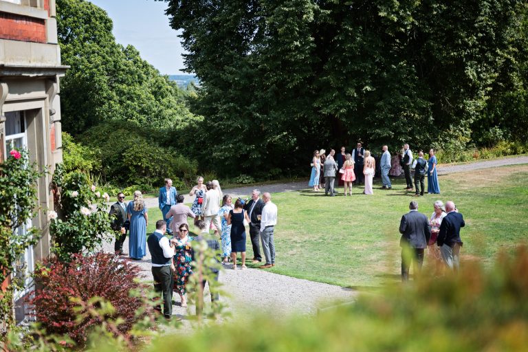 An over view of wedding guest huddle in different groups all chatting on the lawn of a Georgian house.