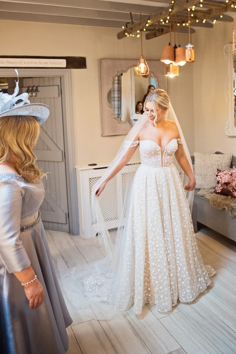 A bride playing with her wedding veil as her mum looks at her admiringly.
