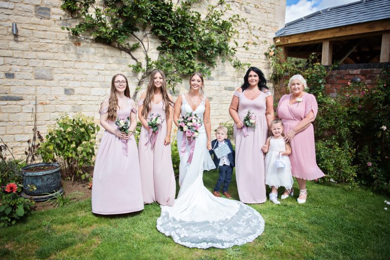 Team bride stand on the lawn with plants and flowers behind them
