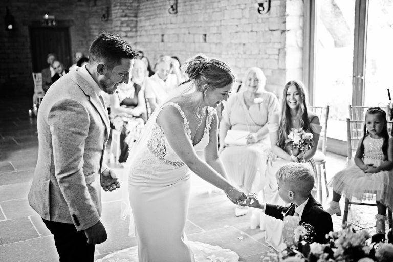 B&W photo of a bride taking the ring from a cute ring bearer during their ceremony at Blackwell Grange