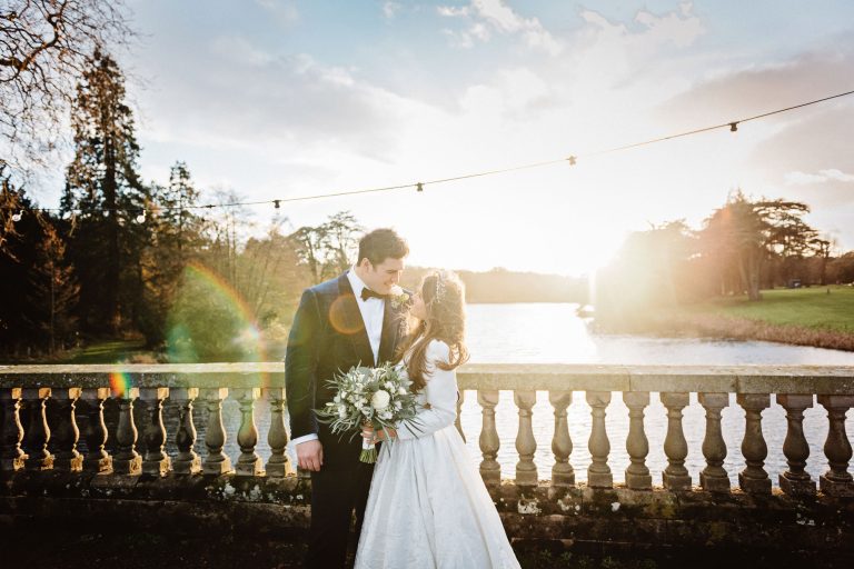 Stunning photo of a bride and groom on the bridge by the lake at Compton Verney - shot at winter with a low sun in the background.