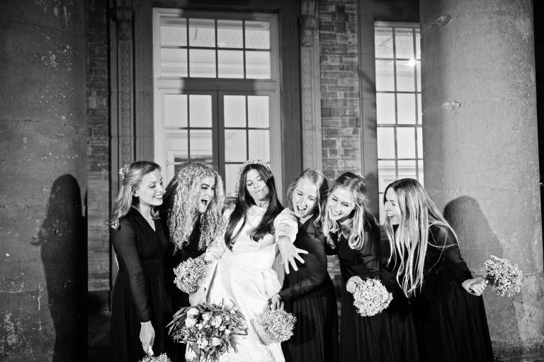 B&W photo of the bridal party outside having fun and looking merry at the brides new wedding ring.