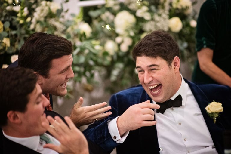 A groom laughing as his friends tell a story.