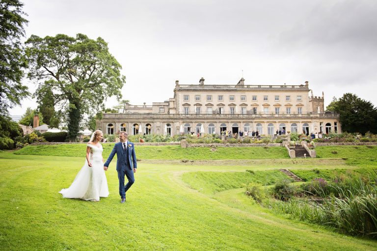 Bride and groom walk hand in hand across the lawn in front of Cowley Manor.