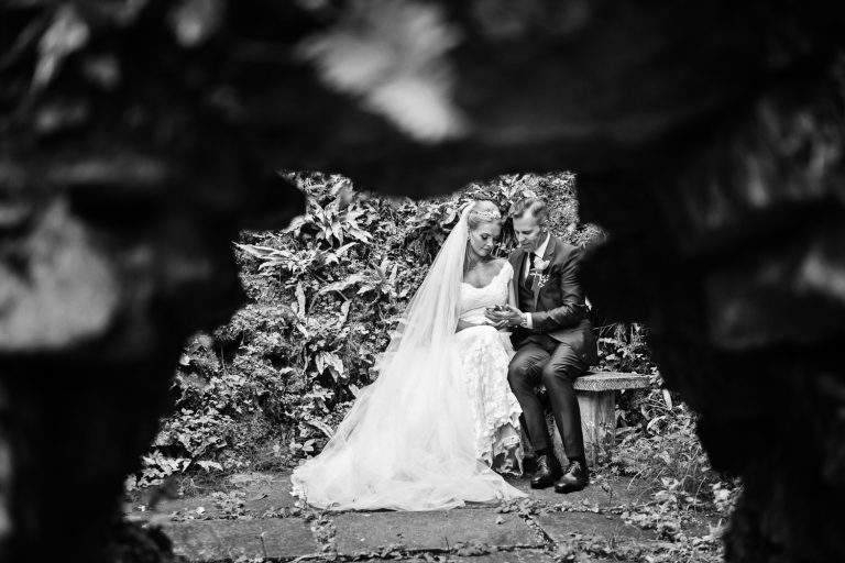 A secret garden at Cowley Manor. Looking through a gap in a wall you see the bride and groom looking at each others wedding rings.