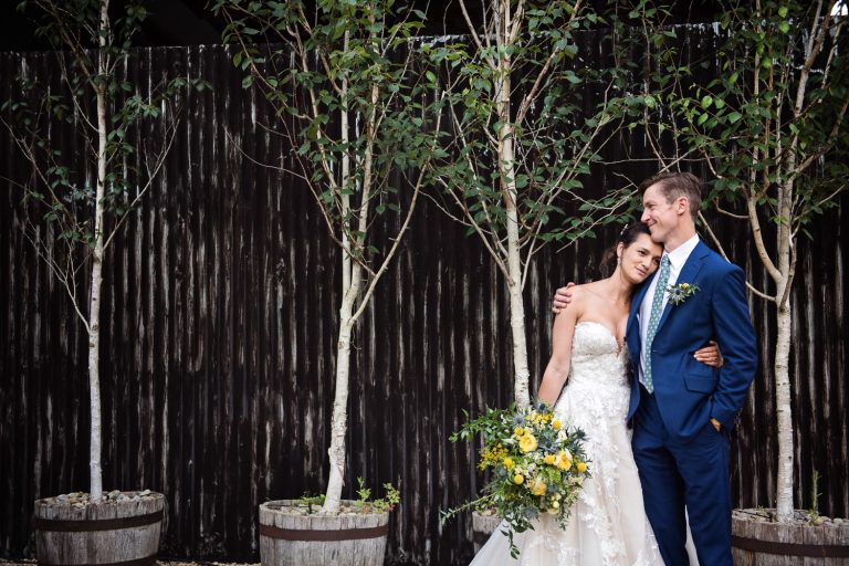 Bride and groom grab a moment together after what is an exhausting day of chatting to friends and family. Background is black metal wall with silver birch tree's.