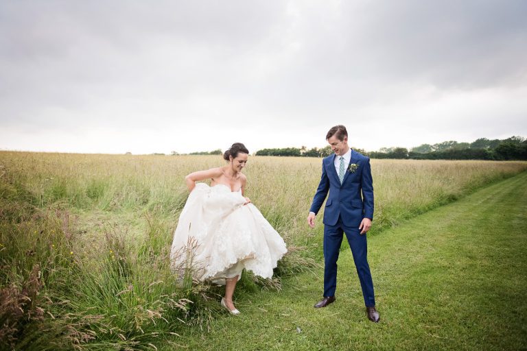 Candid photo of Bride walking through fields with her large wedding dress, groom watching!