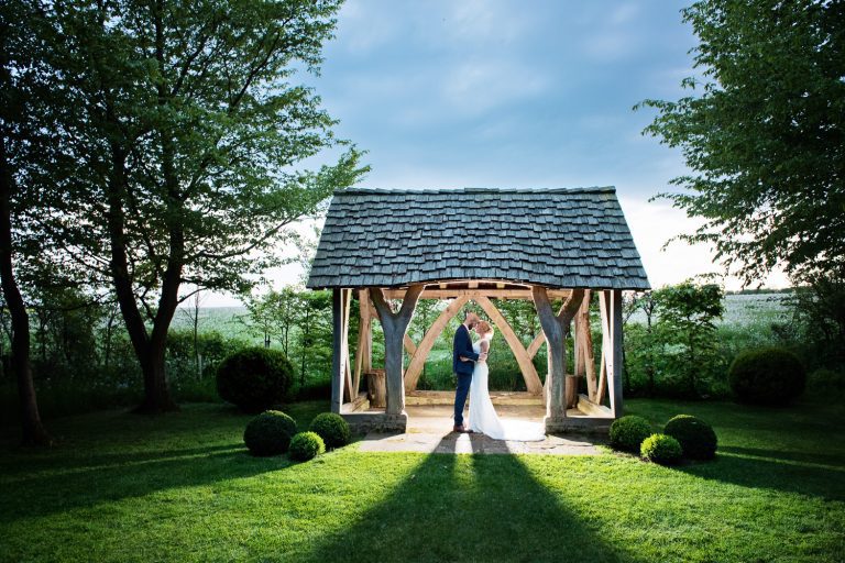 Bride and groom take a moment together in the evening. Little chapel at Cripps Barn lit up whilst couple are close and have their heads together.