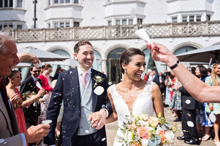 Candid photo of bride and groom being showered with confetti and smiles by their wedding guests.