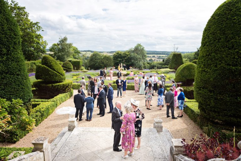 Exterior photograph of wedding guests chatting in the expansive formal grounds at Danesfield house.