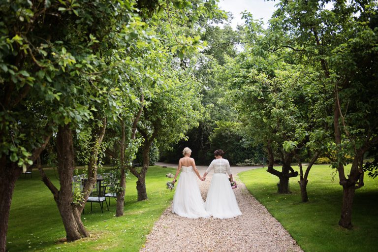 Bride and bride walk hand in hand down the drive away from the camera with tree's either side of them.