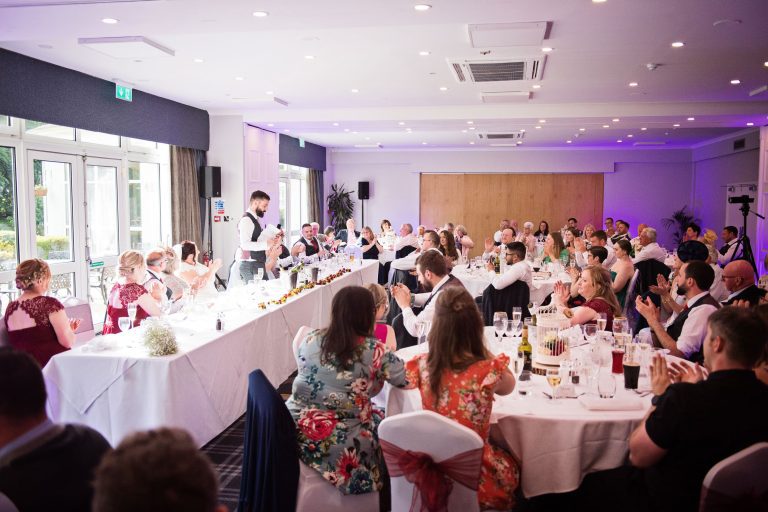 Groom delivering his best man speech in a room at Double Tree Hilton. Wedding guests are clapping in appreciation