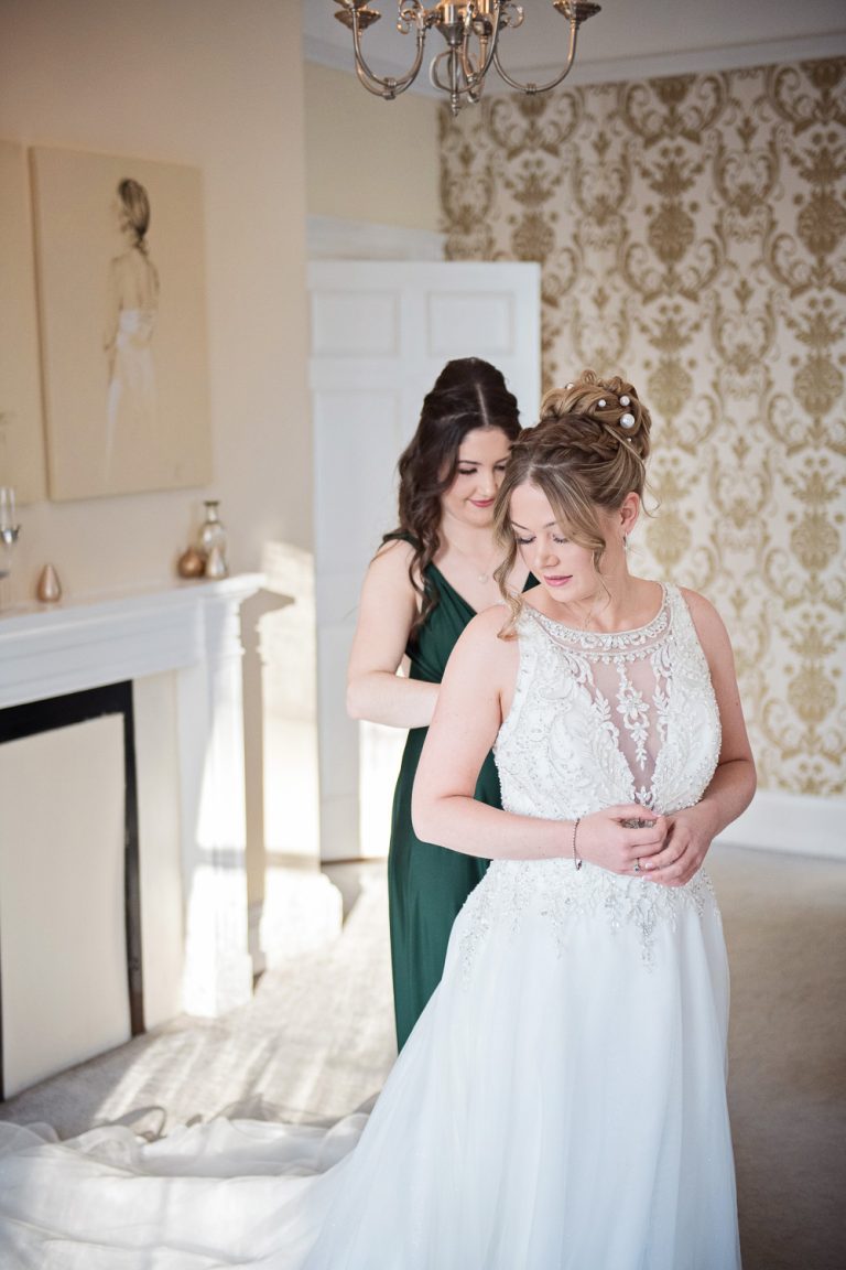 Bridesmaid doing up the brides dress.