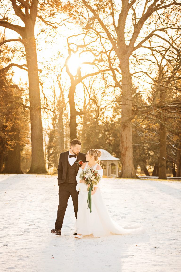 Gorgeous winter portrait photo of bride and groom walking hand in hand during the golden hour at Eastington Park. Snowy backdrop.