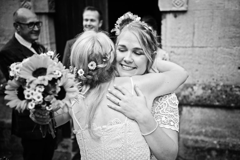 B&W candid photo of bride getting hugged by a friend.