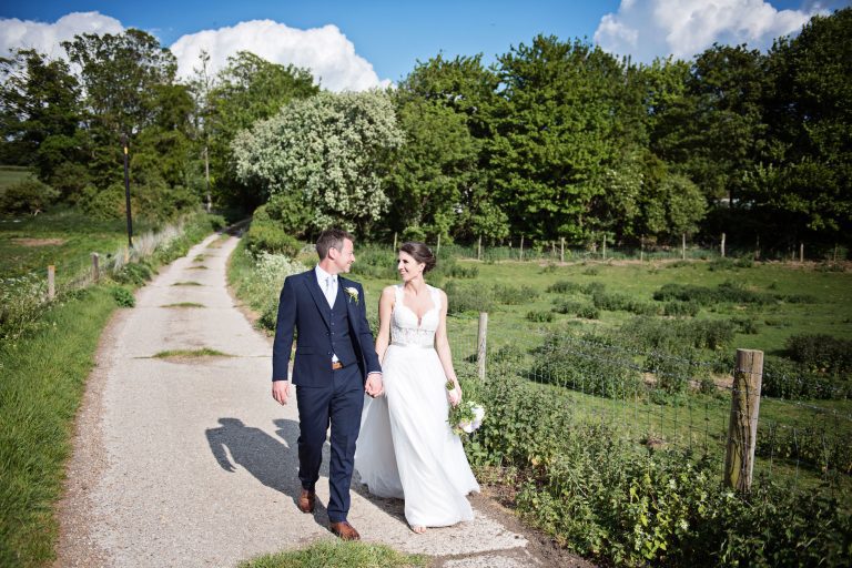 Bride and groom hold hands as they walk in the farmland adjourning Farbridge.