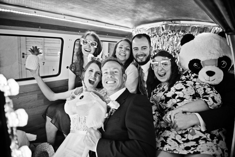 B&W photo of wedding guest and bride and groom smiling and playing whilst they are inside a photo booth.