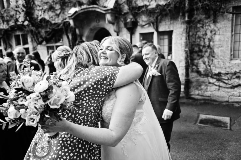 B&W natural image of a bride being hugged by a guest at her wedding.