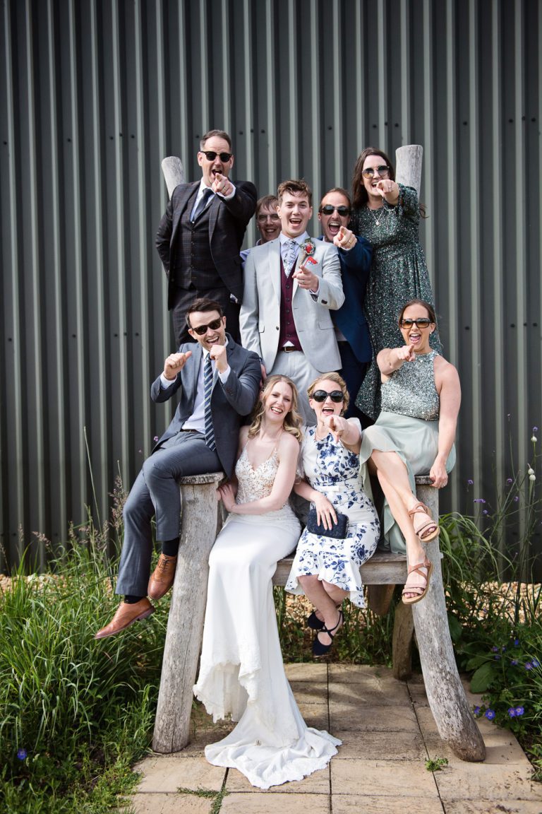 Fun photo of wedding guests on the Giant wooden seat at Huntsmill Farm.