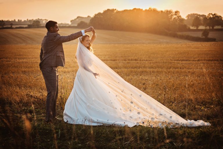 Sunset photo of bride and groom practicing their 1st dance outside on a harvested wheat field.