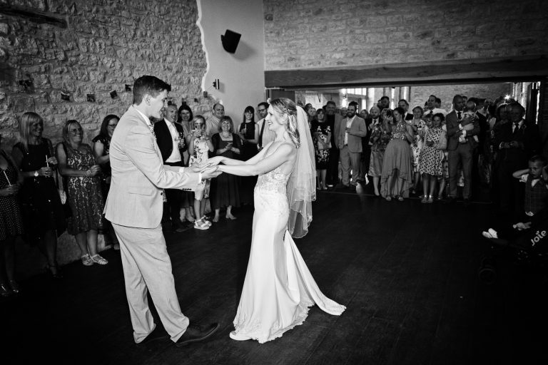 B&W image of bride and groom doing their 1st dance with their friends and family watching.