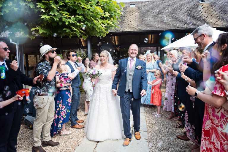 Bride and groom walking in between their guests who are blowing bubbles instead of confetti.
