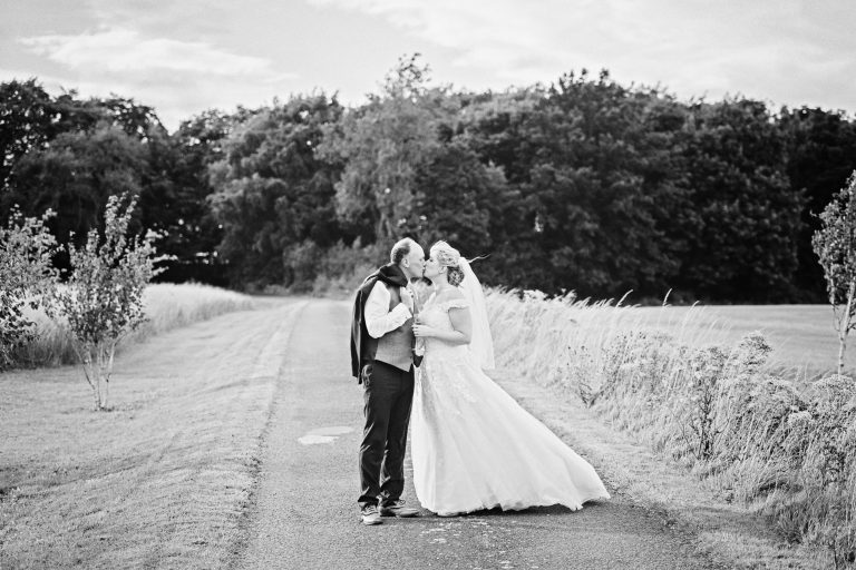 B&W photo of bride and groom kissing in the Cotswold countryside.