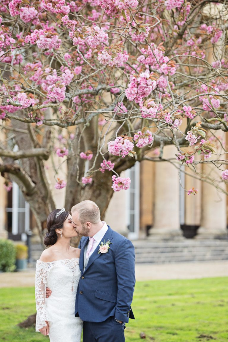 Bride and groom kissing in front of a flowering cherry tree.
