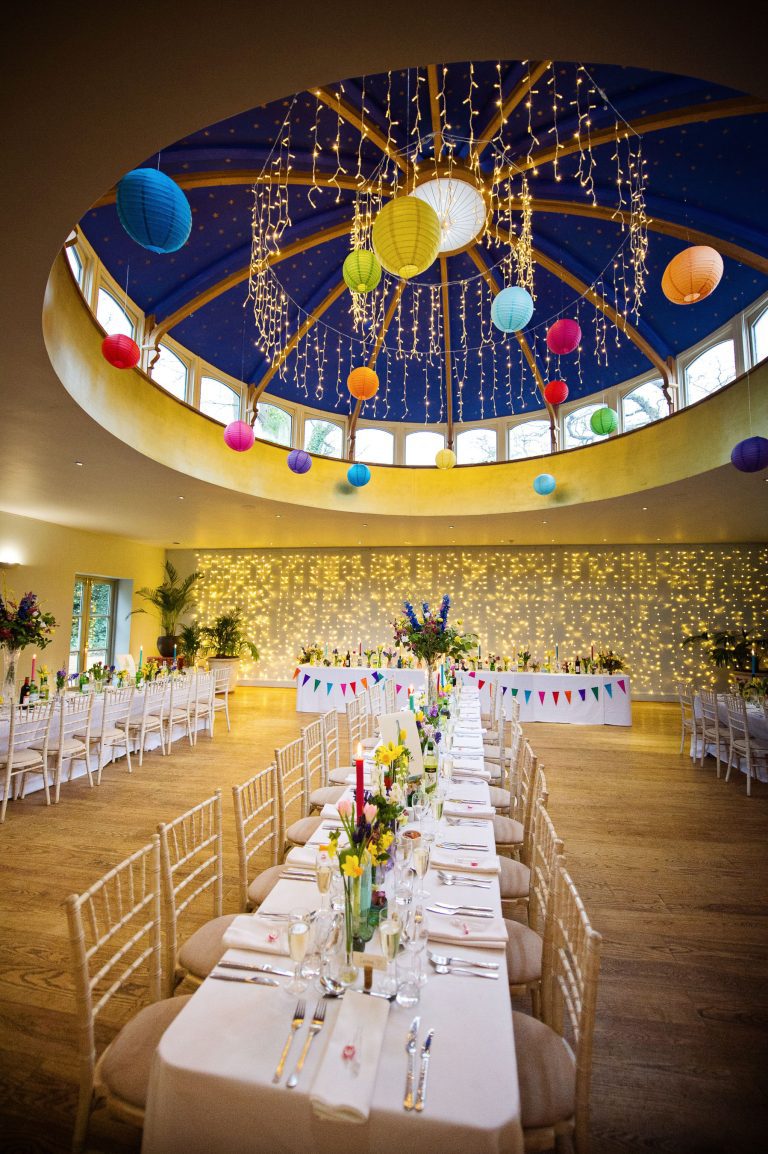 Amazing wide view of a wedding breakfast set up in the Hilarium. Magnificent magical round ceiling above. Fairylights and ceiling balloons make this look out of this world!
