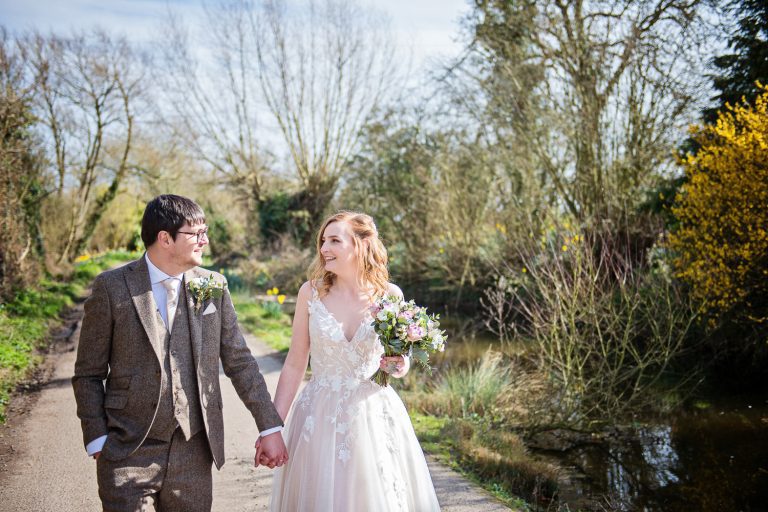 Bride and groom walking hand in hand along a farm track. It's Spring time too!