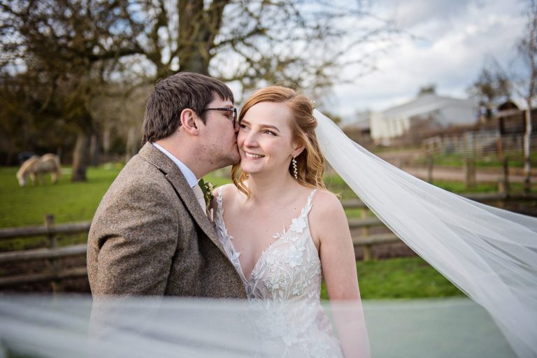 Groom kissing the bride on the cheek, with the brides wedding veil around the camera lens.