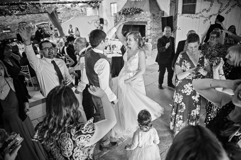 B&W photo of bride and groom dancing, surrounded by their friends and family.