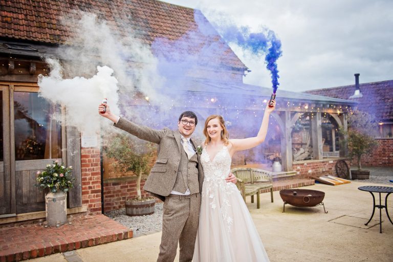 Bride and groom hold smoke bombs in the air outside the front of the wedding barn.