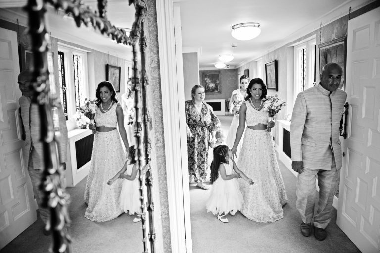 B&W photo of bride walking with her father and flower girl, with a mirror also reflecting the image.